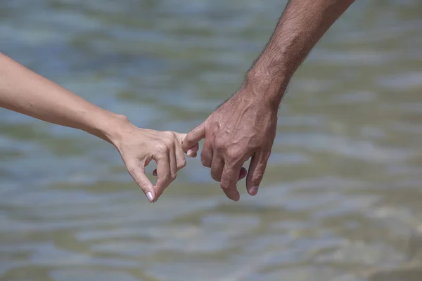 L'homme et la femme gardent pour les mains. Contre l'eau de mer sur la plage, gros plan — Photo