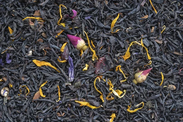Dry herbs tea with fruit and flower petals as background, top view
