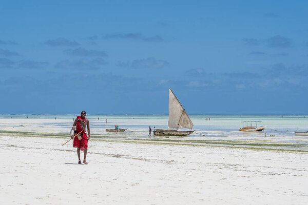 Zanzibar, Tanzania - november 11, 2019 : African man masai dressed in traditional clothes walking near the ocean on the sand beach, Zanzibar, Tanzania, East Africa