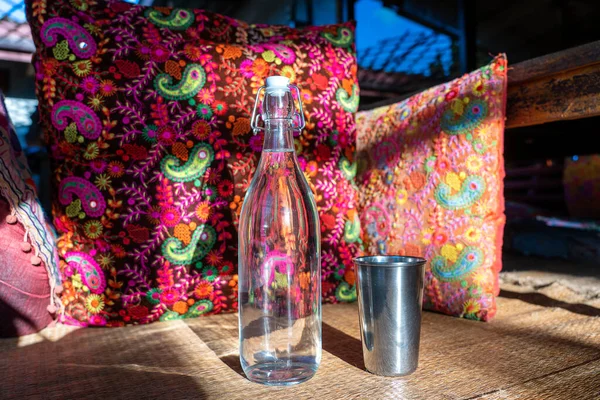 Water bottle on wood table with colorful pillow background in indian cafe, close up