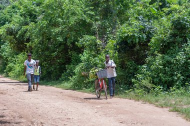 Zanzibar, Tanzanya - 16 Kasım 2019: Güneşli bir günde Tanzanya, Doğu Afrika 'daki Zanzibar adasındaki toprak bir yolda bisikletli bilinmeyen üç Afrikalı adam