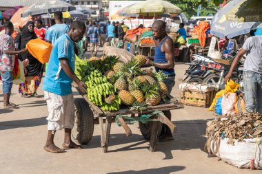 Zanzibar, Tanzanya - 14 Kasım 2019: Afrikalı bir adam Doğu Afrika 'daki Tanzanya' nın Zanzibar adasındaki yerel bir sokak gıda pazarında tropikal meyve arabası taşıyor