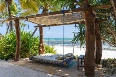 Deniz kenarındaki tropikal plajda, Zanzibar adasında, Tanzanya 'da, Doğu Afrika' da, seyahat ve tatil konseptinde, bir yatak ve yastıkla ahşap salıncak.