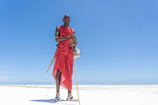 Zanzibar, Tanzania - october 28, 2019 : African man masai dressed in traditional clothes standing near the ocean on the sand beach of Zanzibar island, Tanzania, East Africa