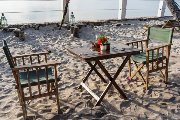 日落时热带沙滩上的木制桌子和两张靠海的椅子 浪漫晚餐的概念 海滩上的户外餐馆 — 图库照片