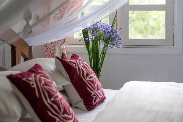 在房间里舒适的柔软的床和一束鲜花靠近窗户 坦桑尼亚 关门了 — 图库照片