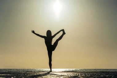 Gün batımında tropik plajda yoga pozu veren kadın silueti. Beyaz kız deniz suyunun yanında yoga yapıyor.