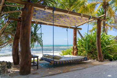 Deniz kenarındaki tropikal plajda, Zanzibar adasında, Tanzanya 'da, Doğu Afrika' da, seyahat ve tatil konseptinde, bir yatak ve yastıkla ahşap salıncak.