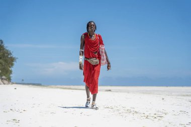 Zanzibar, Tanzanya - 28 Ekim 2019: Geleneksel giysiler içinde Afrikalı adam masai okyanus kenarında, Tanzanya, Doğu Afrika 'daki Zanzibar adasının kumsalında duruyor.