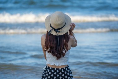 Mavi deniz suyuyla kaplı tropikal plajda güneş şapkası takan Asyalı genç kızın arkası.