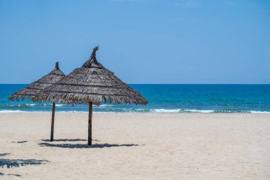 Danang, Vietnam 'da tropik kum plajı ve mavi gökyüzü ve iki saman şemsiyeli yaz denizi suyu. Seyahat ve doğa kavramı