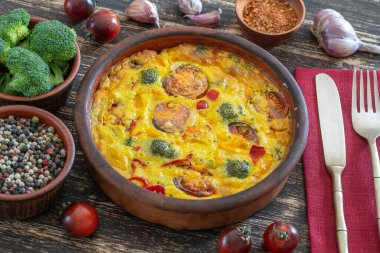 Sebzeli frittata ile seramik kase, basit vejetaryen yemeği. Yumurta, domates, biber, soğan, brokoli ve peynirli frittata, ahşap masaya, yakın çekim. İtalyan omleti.