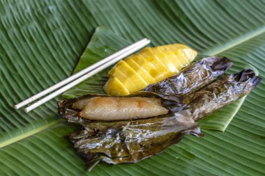 Tayland usulü tatlı, sarı mangolu ve palmiye yapraklı muzlu pilav. Sarı mango ve yapışkan pirinç Tayland 'ın popüler geleneksel tatlısıdır. Kapat.