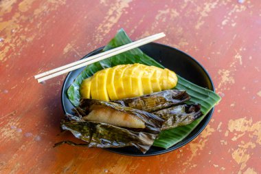 Tayland usulü tatlı, sarı mangolu ve palmiye yapraklı muzlu pilav. Sarı mango ve yapışkan pirinç Tayland 'ın popüler geleneksel tatlısıdır. Kapat.