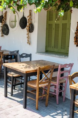 Dışarıdaki küçük kafenin ön manzarası. Beyaz duvarın yanında masa ve boş sandalyeler. Turistik yerler. Tipik Akdeniz restoranı, yazın tatil yapılan bir yer. Kos Adası, Yunanistan