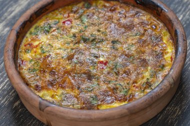 Sebzeli frittata ile seramik kase, basit vejetaryen yemeği. Tahta masada domates, biber, soğan ve peynirli frittata, yakın çekim. İtalyan omleti, üst manzara.