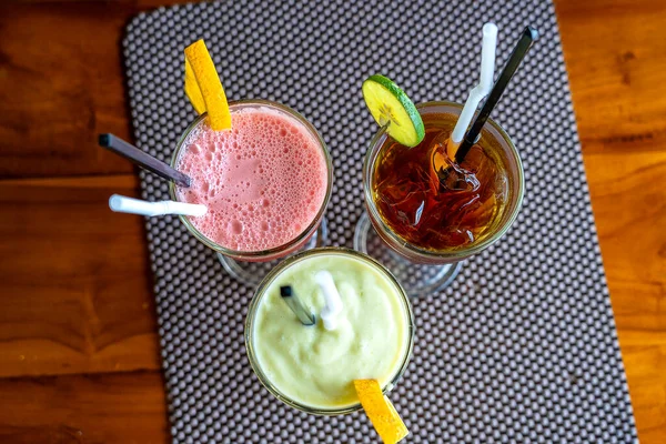 Avocado smoothie, watermelon shake and cold tea in a glass on a wooden table. Tropical drink concept . Top view, close up