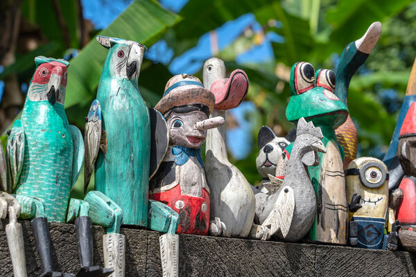 Старые деревянные сувенирные игрушки на каменном заборе возле кукольного магазина в Убуде, остров Бали, Индонезия. Закрыть