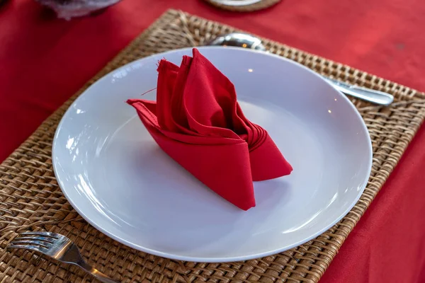 Elegant table setting with fork, spoon, white plate and red napkin in restaurant , close up. Nice dining table set with arranged silverware and napkins