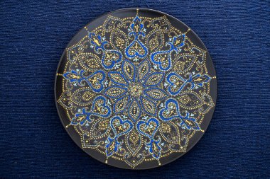 Dekoratif seramik plaka, siyah, mavi ve altın renkli, arka planda boyanmış, yakın plan, üst manzara. Akrilik boyalarla boyanmış dekoratif porselen tabaka, el işi, nokta boyası.