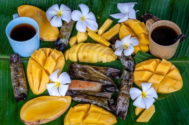 Tayland usulü tatlı, sarı mangolu ve palmiye yapraklı muzlu pilav. Sarı mango ve yapışkan pirinç Tayland 'ın popüler geleneksel tatlısıdır. Kapat.