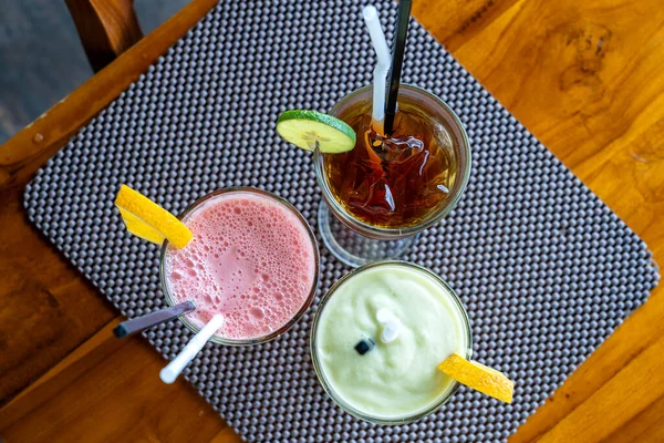 Avocado smoothie, watermelon shake and cold tea in a glass on a wooden table. Tropical drink concept . Top view, close up