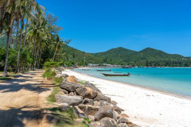 Toprak yolu, mavi deniz suyu, hindistan cevizi palmiyeleri ve tekneleri olan güzel bir koy. Tayland 'daki Koh Phangan adasında tropik kum plajı ve deniz suyu.