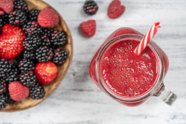 Beyaz masada cam bardakta taze organik kırmızı smoothie, yakın plan, üst manzara. Yaz meyvelerini tazeliyorum. Sağlıklı beslenme kavramı. Böğürtlen, ahududu ve çilekli smoothie
