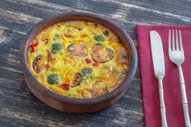 Sebzeli frittata ile seramik kase, basit vejetaryen yemeği. Yumurta, domates, biber, soğan, brokoli ve peynirli frittata, ahşap masaya, yakın çekim. İtalyan omleti.