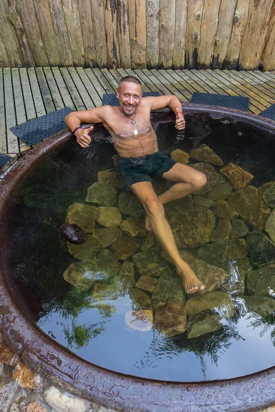 Man bathing in cast iron vat with mineral water containing hydrogen sulphide. Water in cast iron vats heated to 45 degrees Celsius. Ukraine, Carpathian region. Concept of travel and healthy lifestyle