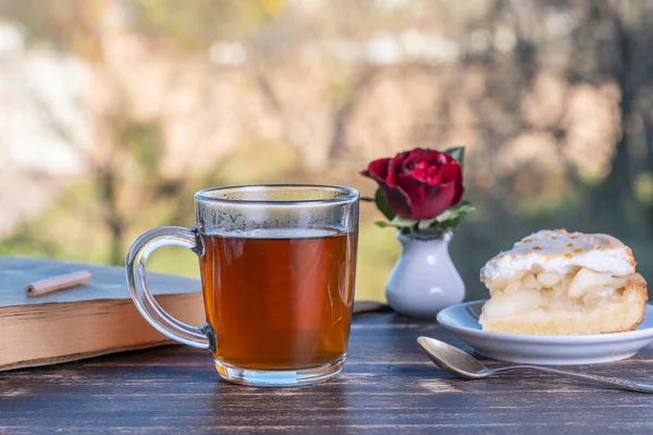 Tea glass with sweet cake and book on wooden table in the morning, outdoors, close up