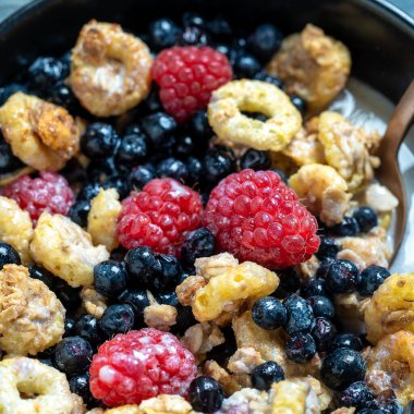 Siyah bir kasede ahududu, yaban mersini ve taneli müsli, yakın çekim. Sağlıklı yemek, sağlıklı kahvaltı konsepti
