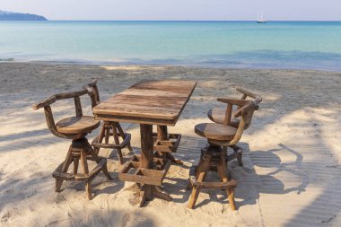 Tahta kafe masası ve arka planda mavi deniz olan tropikal bir plajda sandalyeler, Tayland. Tatil ve yaz konsepti