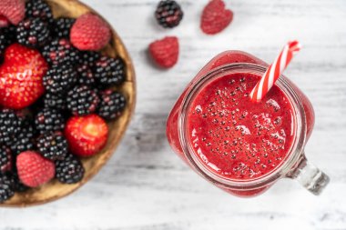 Beyaz masada cam bardakta taze organik kırmızı smoothie, yakın plan, üst manzara. Yaz meyvelerini tazeliyorum. Sağlıklı beslenme kavramı. Böğürtlen, ahududu ve çilekli smoothie