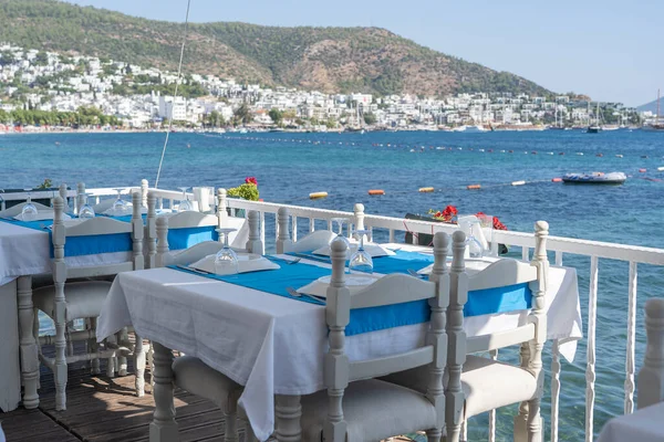 Elegant table setting with fork, knife, wine glass, white plate and blue napkin in restaurant. Nice dining table set with arranged silverware and napkin for dinner, Bodrum, Turkey. Beach cafe near sea