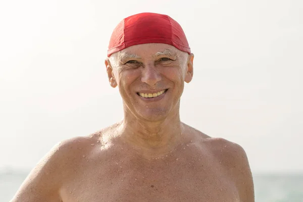 在靠近海水的海滩上 戴着红色游泳帽的快乐老人 — 图库照片