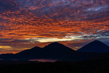 Batur ve Agung volkanlarında, Kintamani 'de, Bali adasında, Endonezya' da gündoğumunda. Agung Dağı 'nın tepesinden güneşin doğuşu volkan manzarası, doğa manzarası. Volkanik dağların siluetiyle bulutlu bir manzara.
