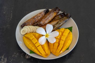 Tayland usulü tatlı, sarı mangolu ve palmiye yapraklı muzlu pilav. Sarı mango ve yapışkan pirinç Tayland 'ın popüler geleneksel yemeğidir. Kapat.