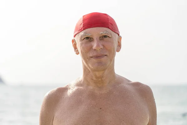 Deniz Suyunun Yanındaki Kumsalda Kırmızı Yüzme Şapkalı Mutlu Yaşlı Adam — Stok fotoğraf