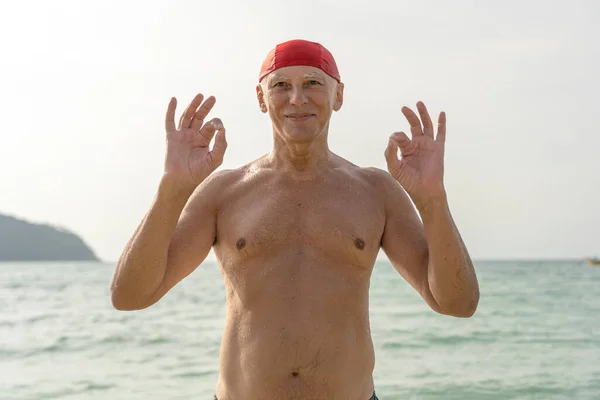 在靠近海水的海滩上 戴着红色游泳帽的快乐老人 — 图库照片