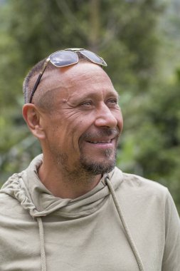 İnsanlar ve yaşam tarzı konsepti. Yeşil doğa geçmişine karşı orta yaşlı, traşsız, mutlu bir adam. Yetişkin adam portresi. Yakından.