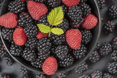 Taze organik böğürtlen ve ahududu arkaplanı, yakın plan. Bir sürü olgun, sulu, siyah tabakta çiğ meyve. Üst manzara böğürtlen ve ahududu