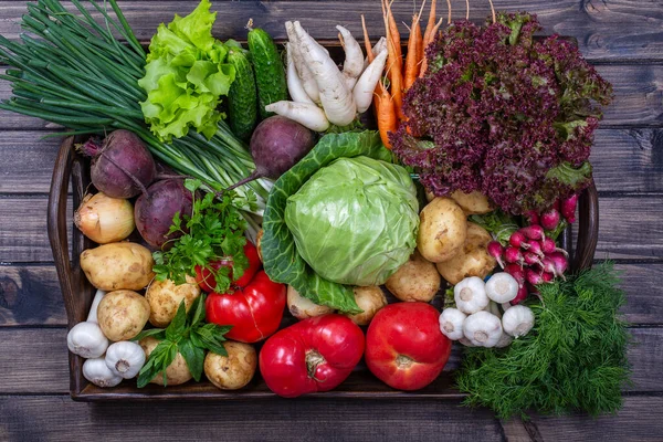 Mixed vegetables on a wooden tray, close up. Fresh vegetables in wooden tray. Healthy food ingredients. Organic farmer vegetables. Top view.