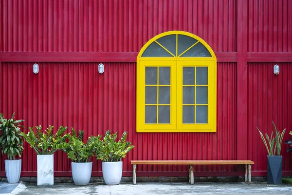 Yellow window, flowerpots with plants and bench on the background of a red metal wall on the street of Danang city in Vietnam, close up