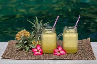 Ev yapımı mango ve hindistan cevizi sütüyle yapılmış ananas püresi yüzme havuzunun yanındaki cam bardakta, yakın plan. Endonezya, Bali Adası. Tropikal meyve içeceğini tazeliyorum. Sağlıklı beslenme kavramı.