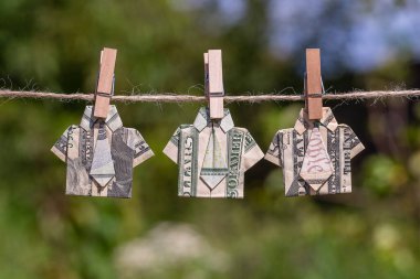 Asılı yeşil doğa üzerine dolar banknotundan yapılmış Origami gömleği. İpe asılmış dolar banknotları. Kapatın. Dolar Tişörtü