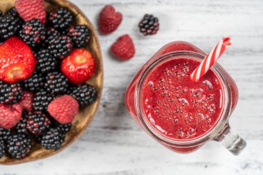 Beyaz masada cam bardakta taze organik kırmızı smoothie, yakın plan, üst manzara. Yaz meyvelerini tazeliyorum. Sağlıklı beslenme kavramı. Böğürtlen, ahududu ve çilekli smoothie