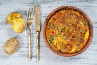 Sebzeli frittata ile seramik kase, basit vejetaryen yemeği. Tahta masada domates, biber, soğan ve peynirli frittata, yakın çekim. İtalyan omleti, üst manzara.