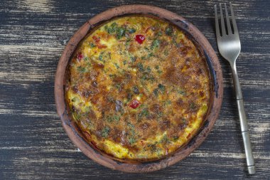 Sebzeli frittata ile seramik kase, basit vejetaryen yemeği. Tahta masada domates, biber, soğan ve peynirli frittata, yakın çekim. İtalyan omleti, üst manzara.