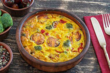 Sebzeli frittata ile seramik kase, basit vejetaryen yemeği. Yumurta, domates, biber, soğan, brokoli ve peynirli frittata, ahşap masaya, yakın çekim. İtalyan omleti.